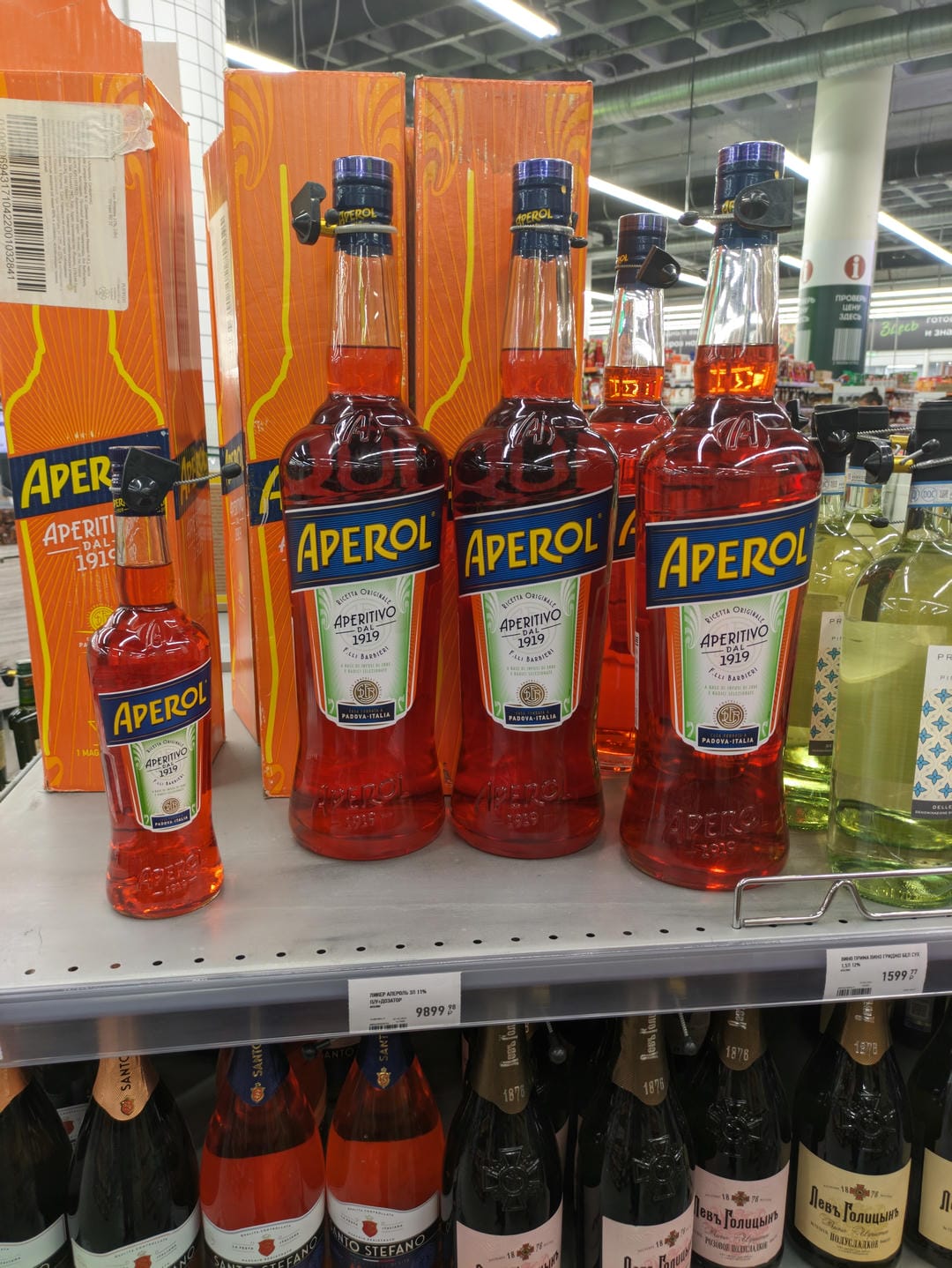 Several bottles of orange Aperol liquor displayed on supermarket shelves.