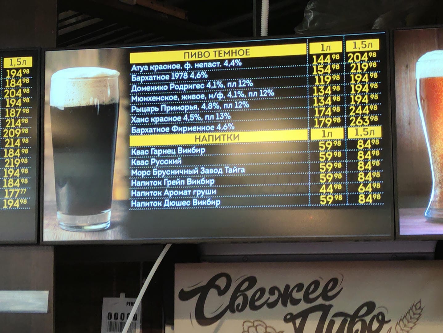 An electronic screen displaying prices of different kinds of drinks, with a glass of dark beer beside it.