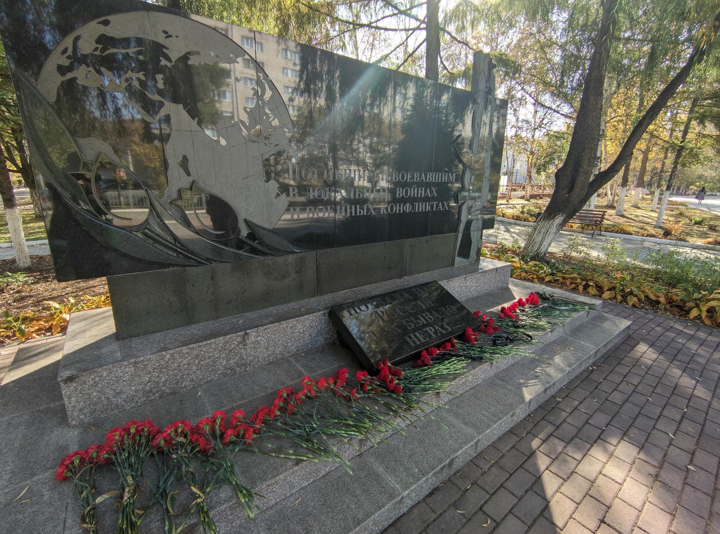 A black monument engraved with text, surrounded by red flowers.