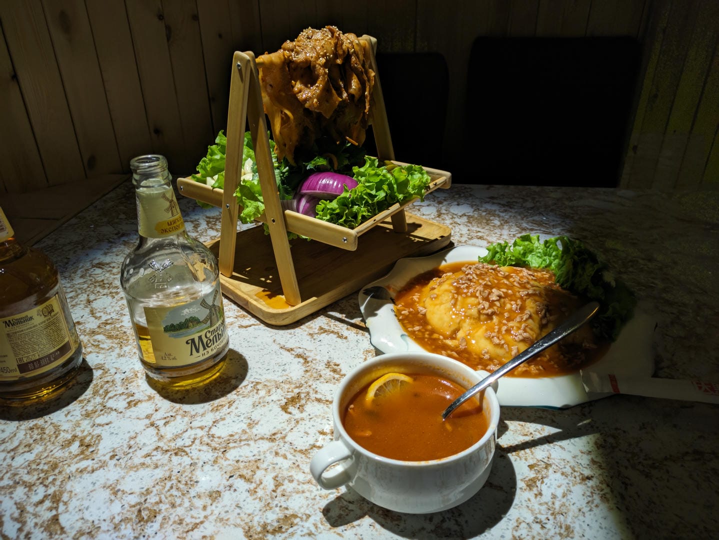 A dining table set with a bowl of soup, a meat dish, and a bottle of wine.
