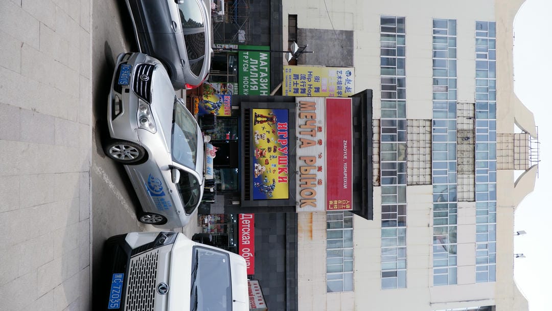 A multi-story building with multiple windows on the front. Below it, there is a sign that reads “МЕЧТА РЫНОК,” and there are other shop signs nearby.