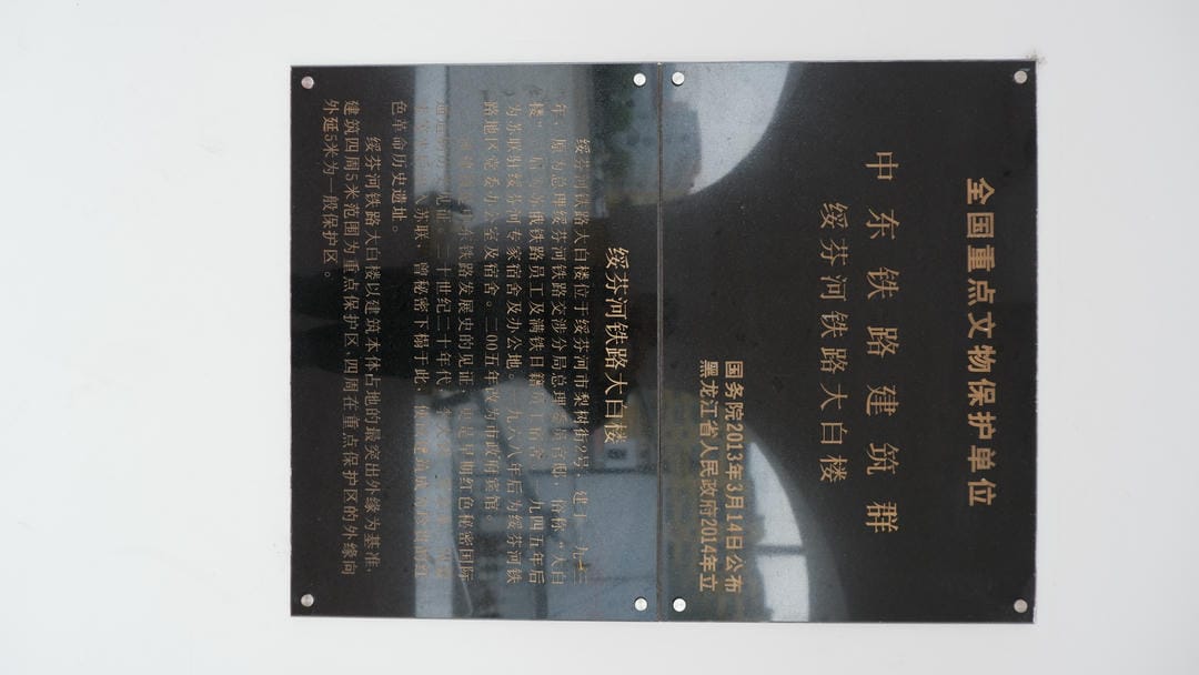 A black metal plaque with Chinese text stating “National Key Cultural Heritage Protection Unit” and information about the “Middle East Railway Architecture Cluster Suifenhe Railway White Building.”