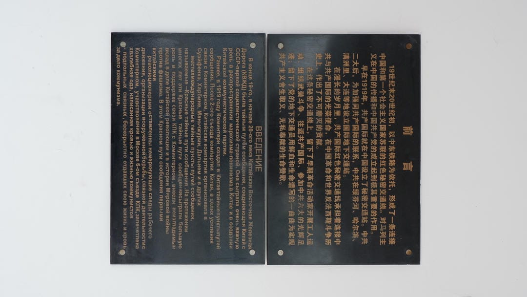Two black metal plaques, one written in Chinese above and another in Russian below, providing historical information about a building.