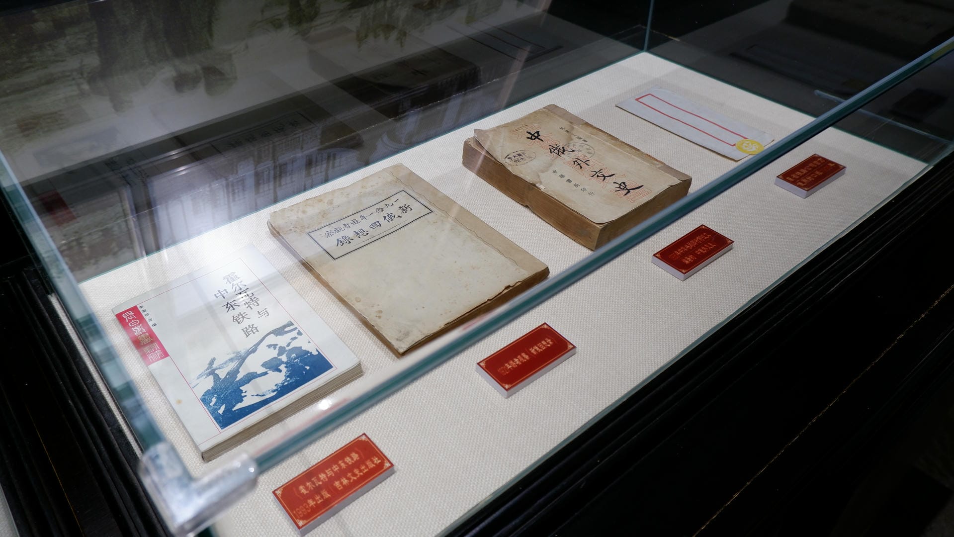 A glass display case contains old books and documents, accompanied by red labels for explanation.