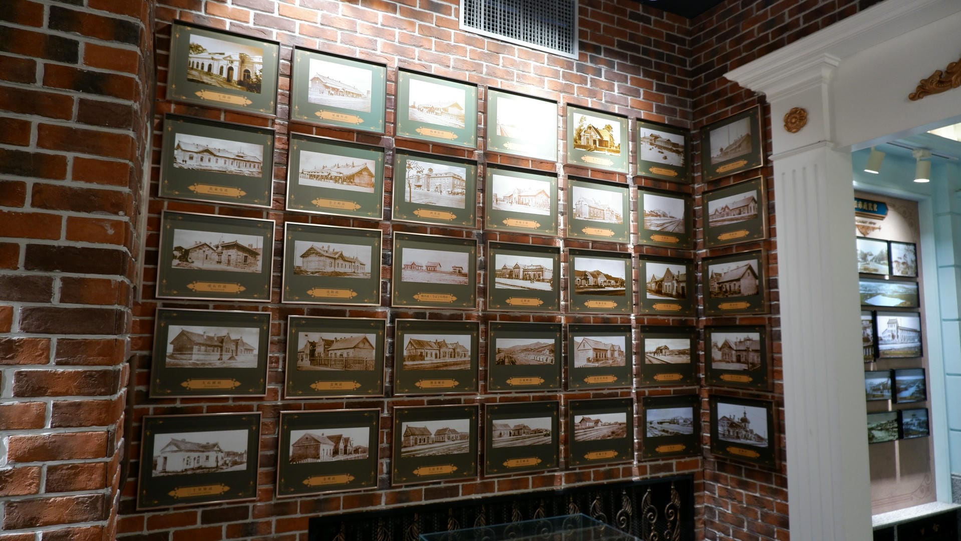 A dense arrangement of framed historical photos hangs on a red brick wall, with a white column on the right.