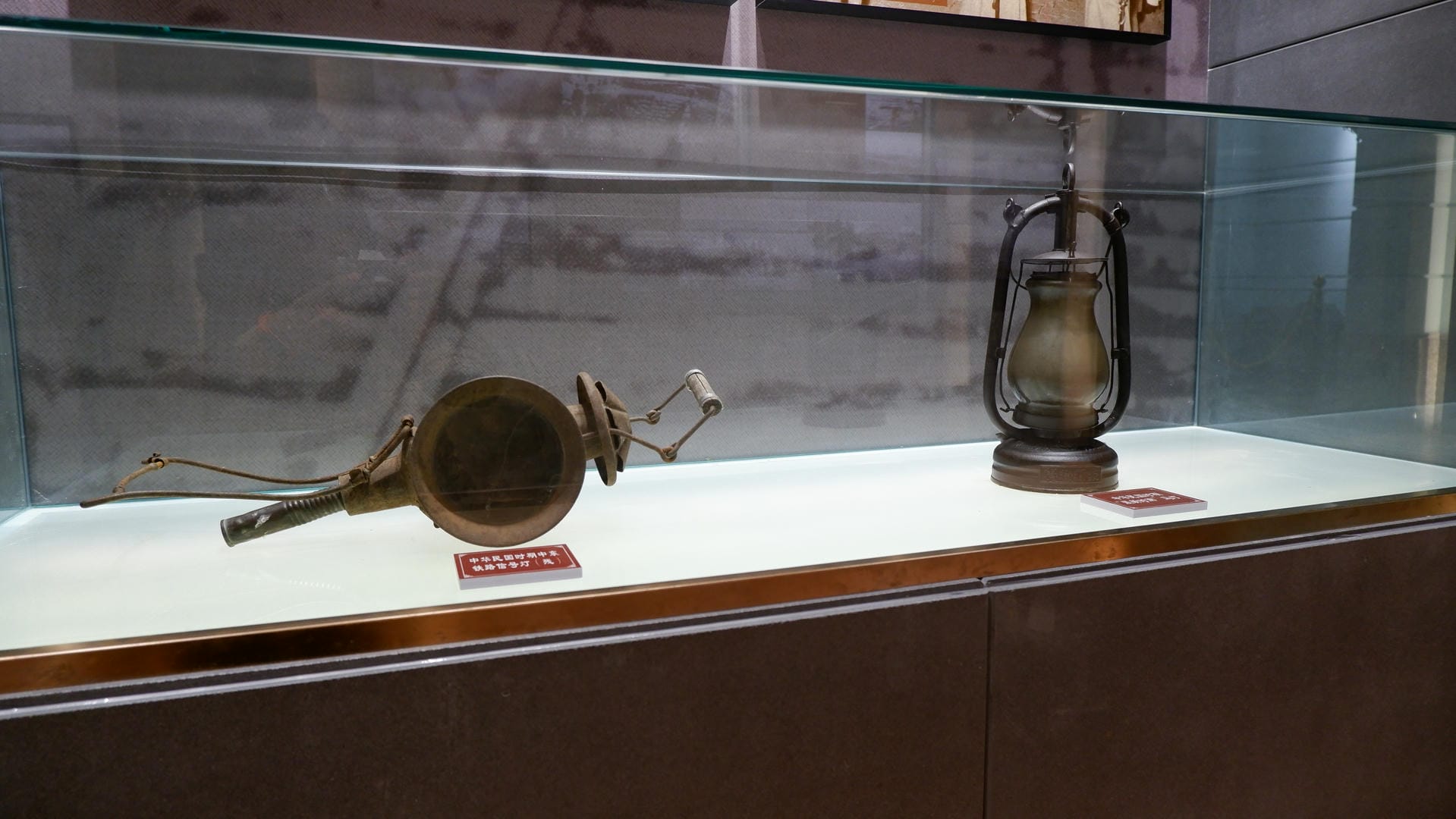 A copper horn and a kerosene lamp are displayed in a glass case.