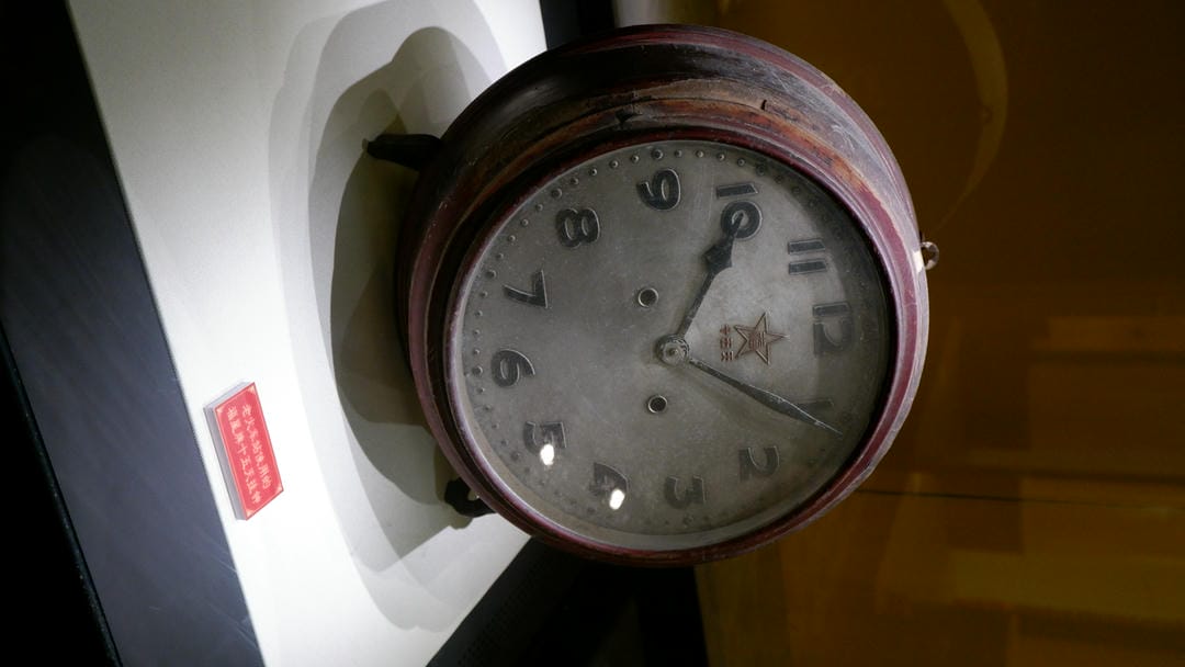 An old clock with numbers and hands sits on a white base.