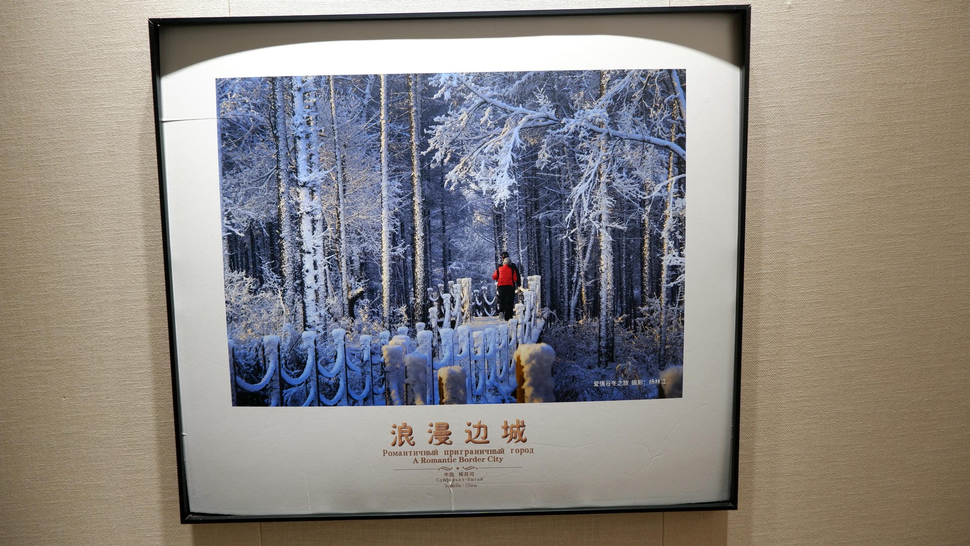 A painting depicts trees in the snow, with a person wearing red clothes.