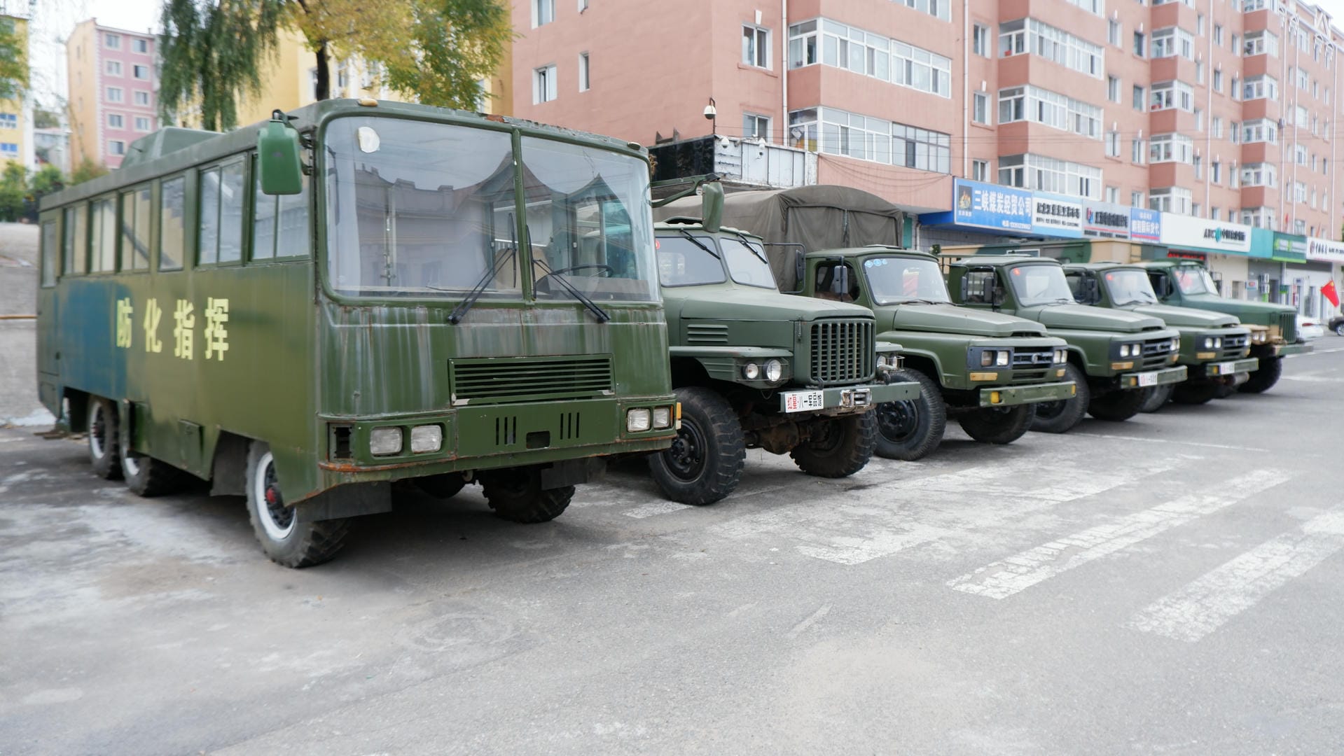 A row of green military buses and trucks are parked in a lot, with Chinese markings on the vehicles.