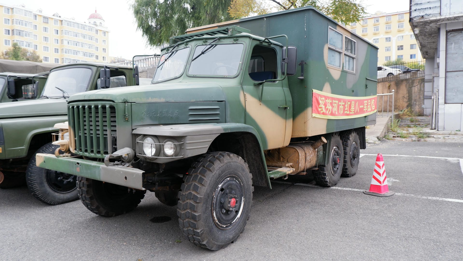 A green military truck is parked in a lot, with Chinese slogans on its body.