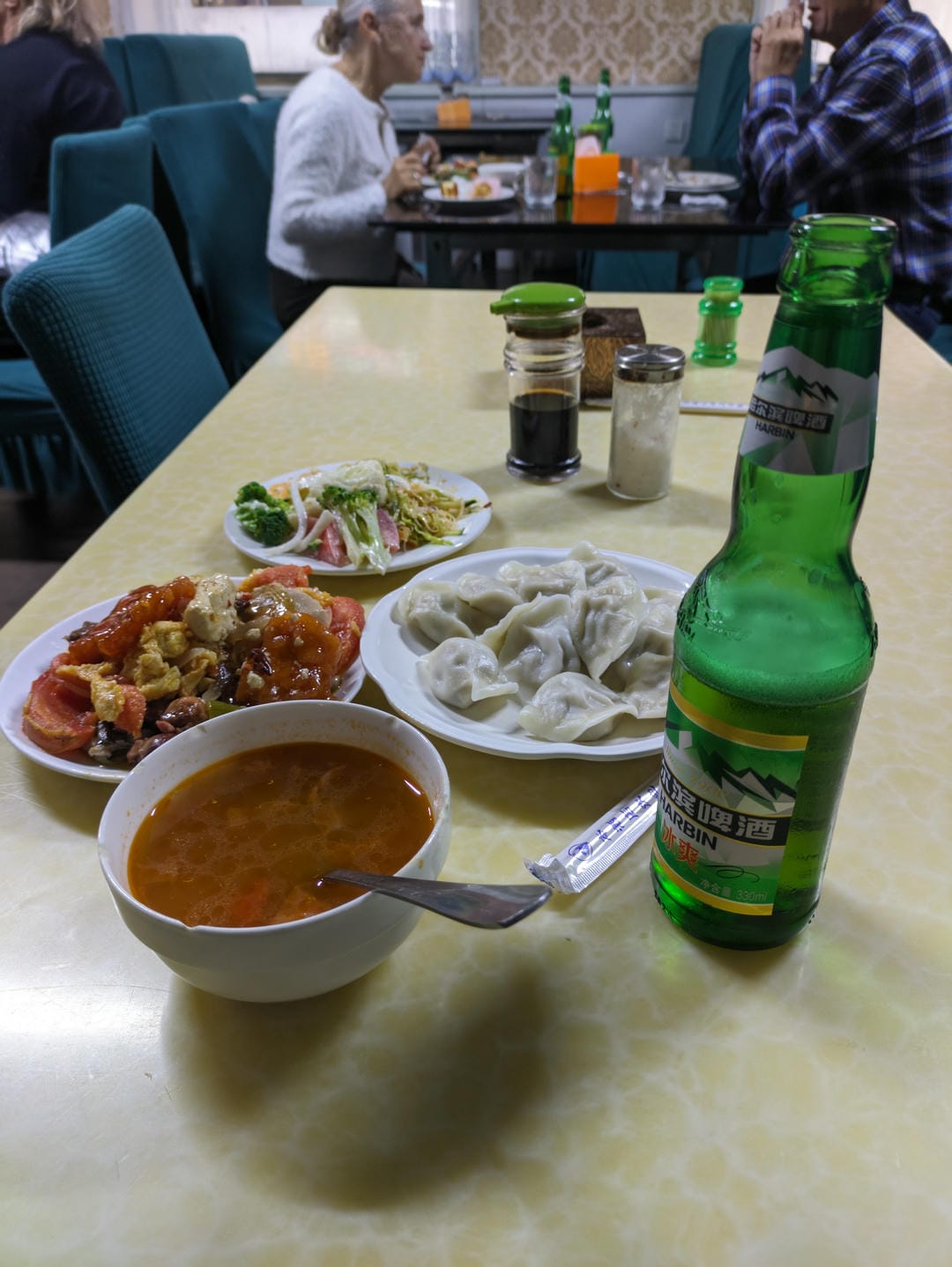 Dumplings, stir-fried dishes, soup, and a bottle of beer are laid out on a dining table.