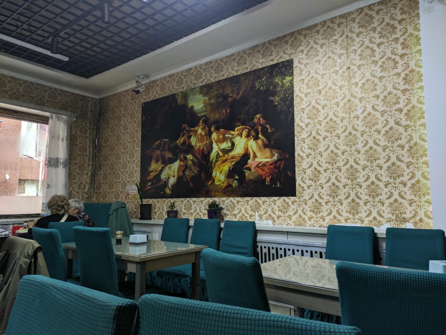 A large oil painting depicting a classical scene hangs on the wall inside a restaurant.