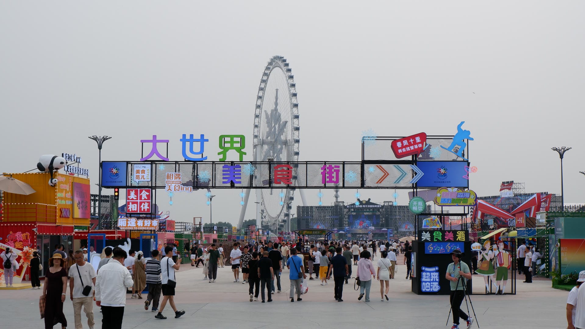 people walking around a city plaza with a ferris wheel in the background
