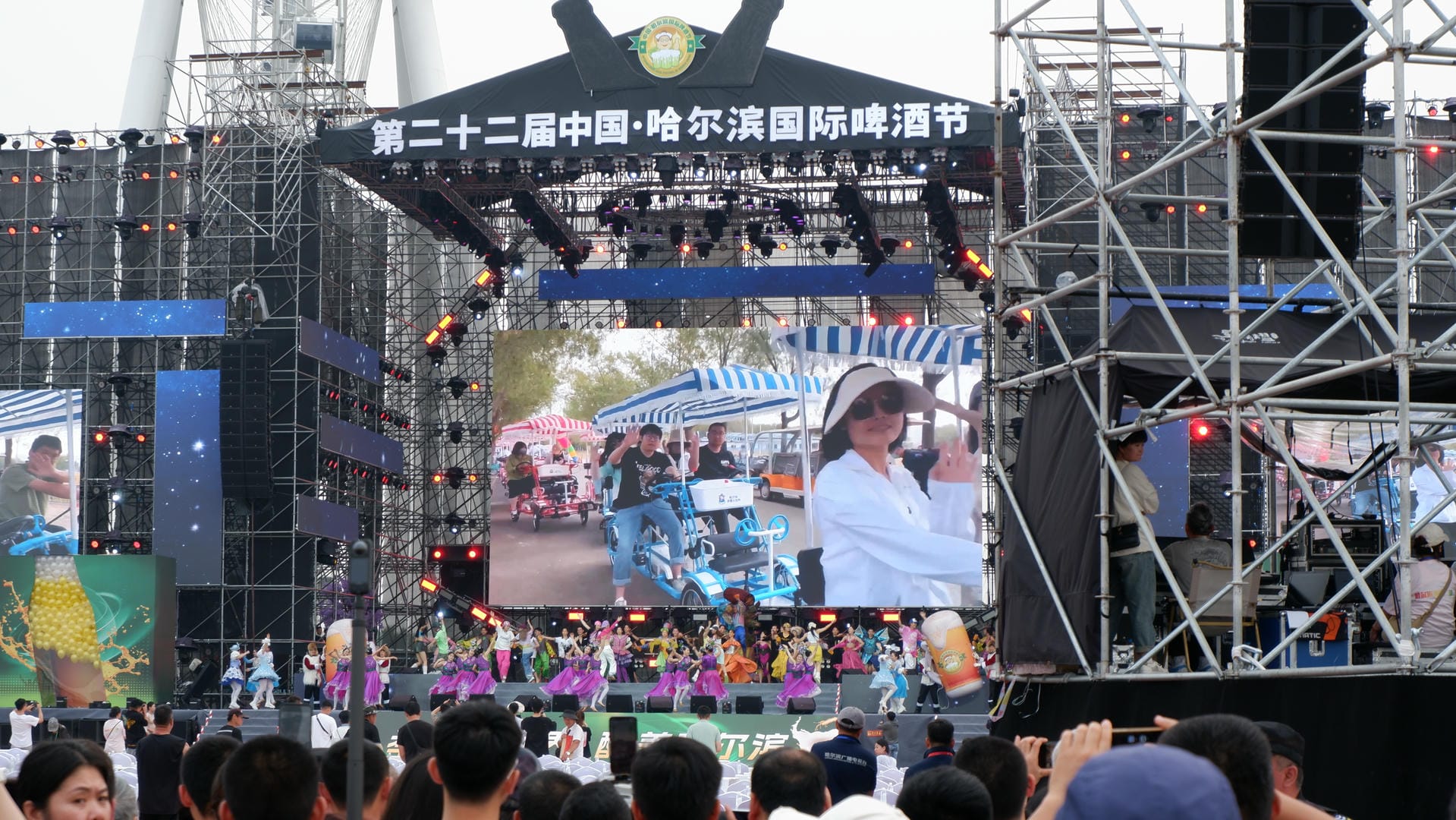 there are many people standing in front of a stage with a large screen
