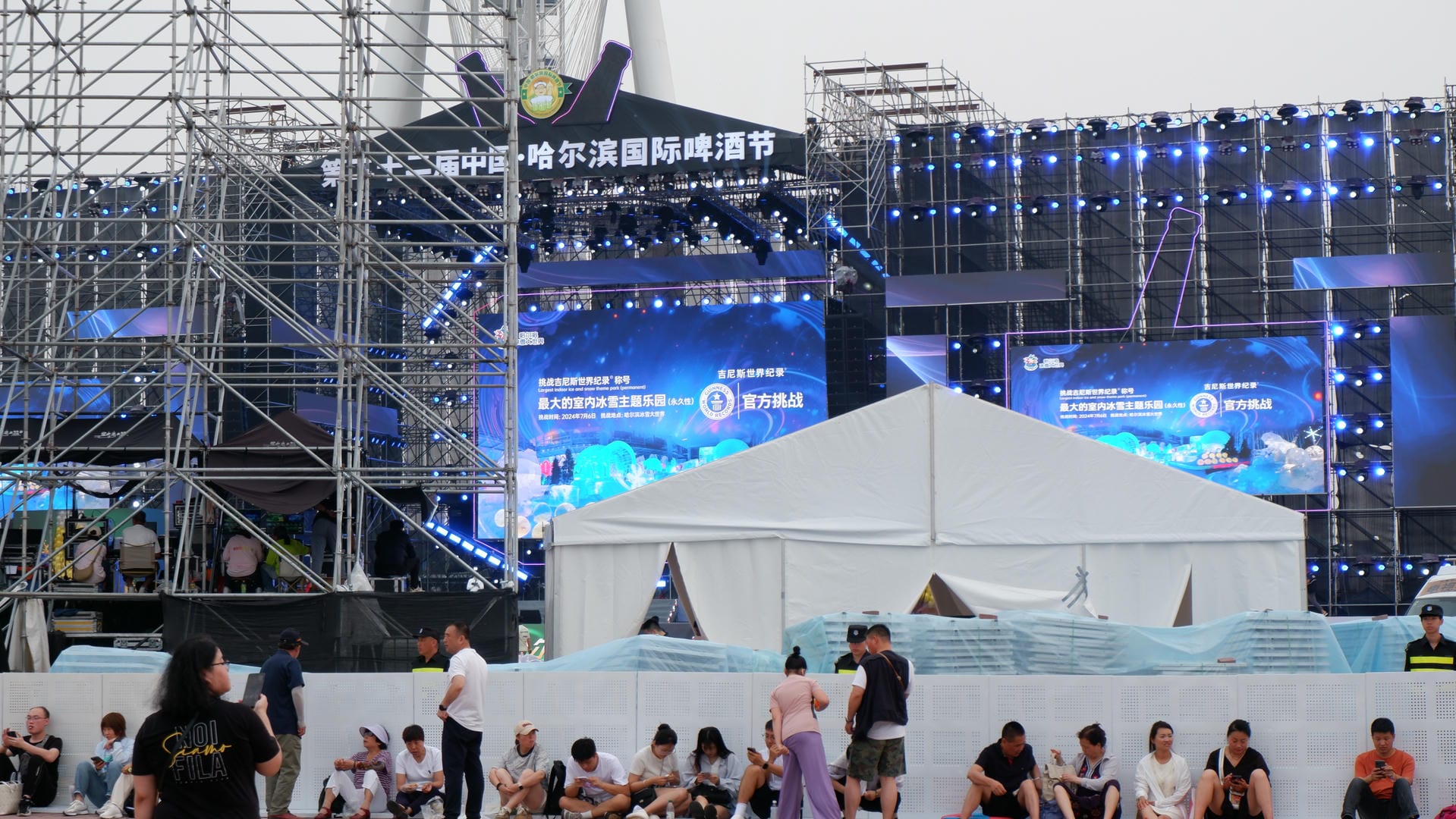 people sitting on the ground in front of a stage with a large screen
