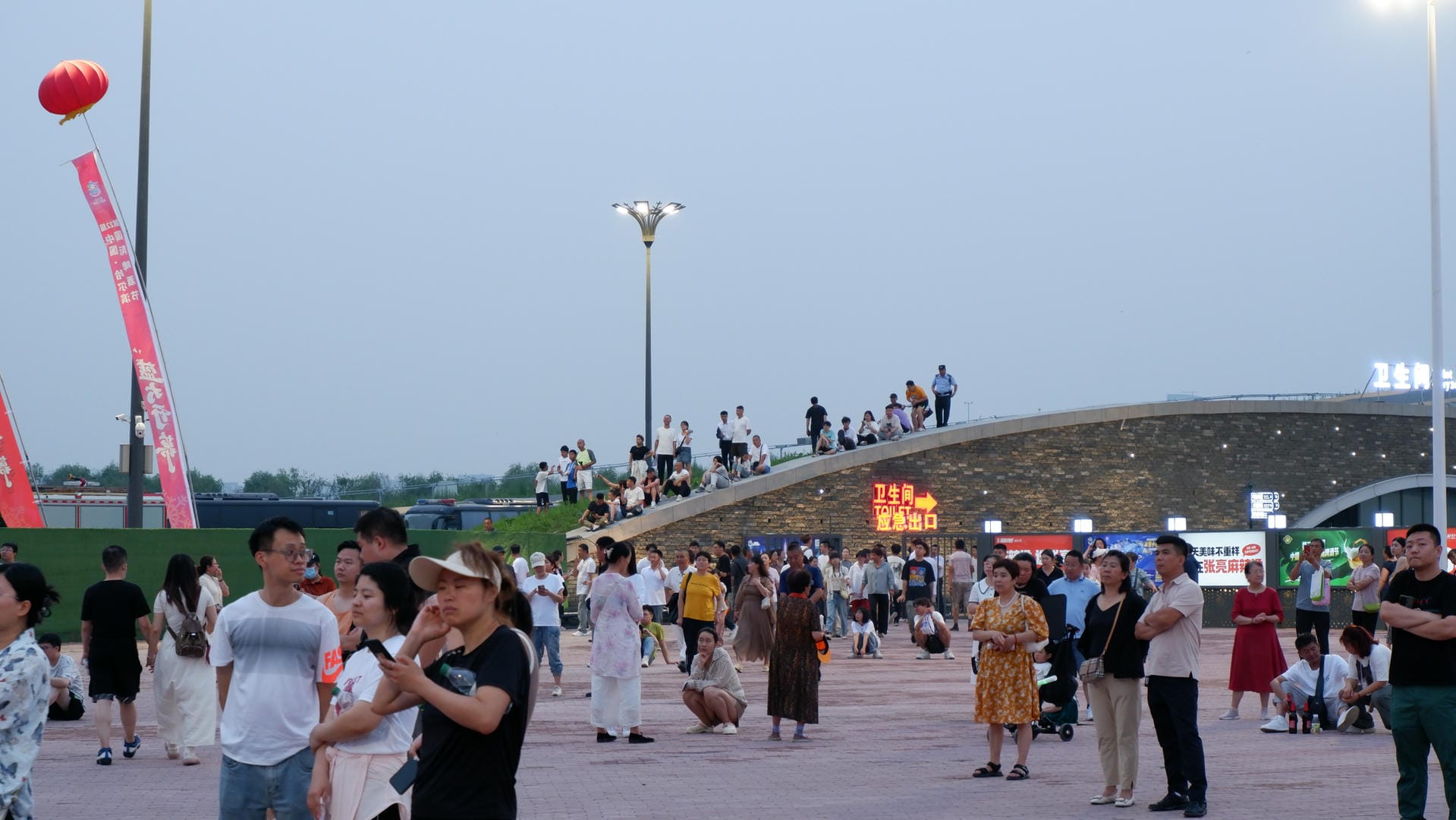 people are standing in a plaza with a bridge and a red lantern