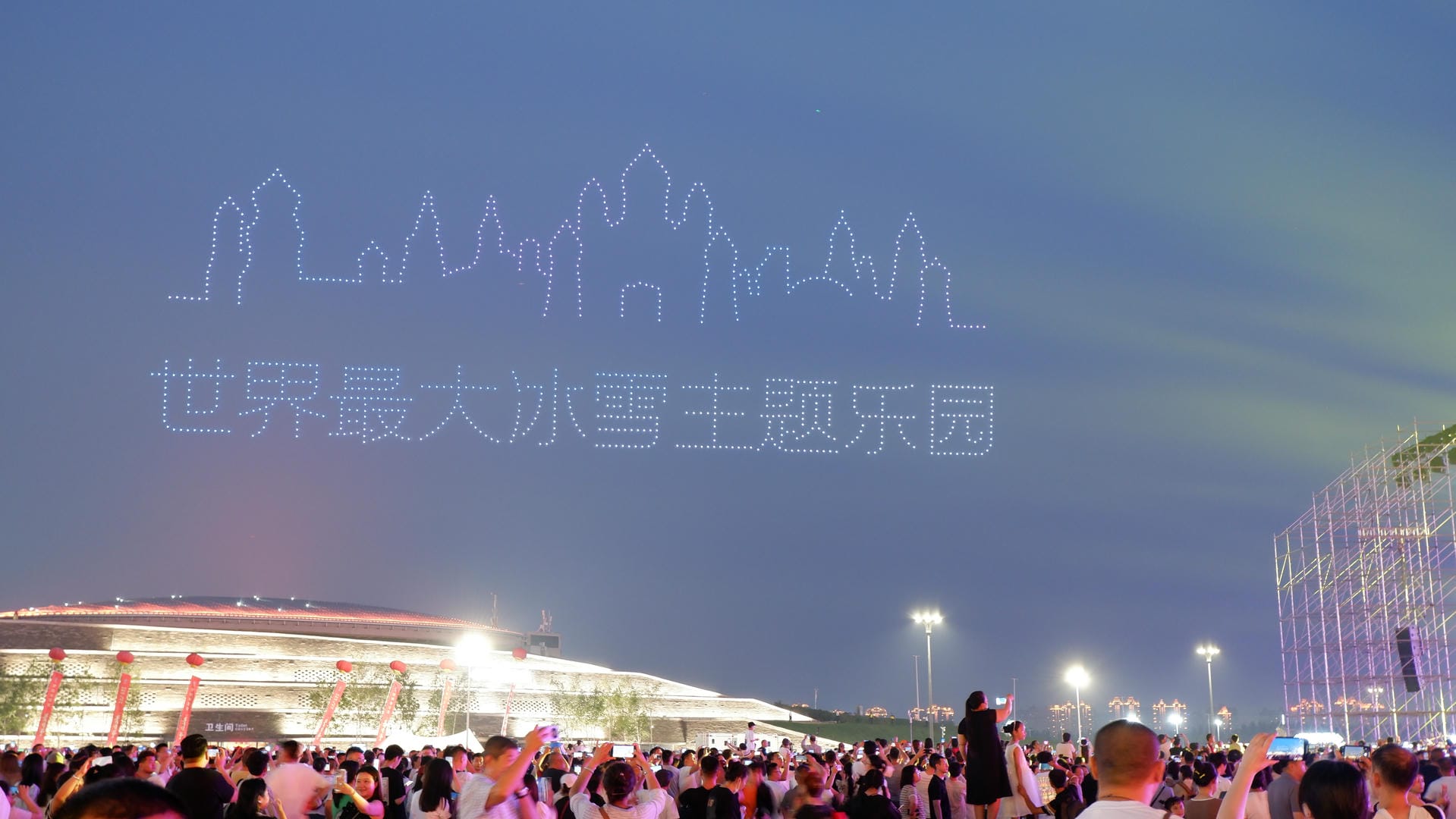 people are gathered in a large crowd at night with lights projected on the sky