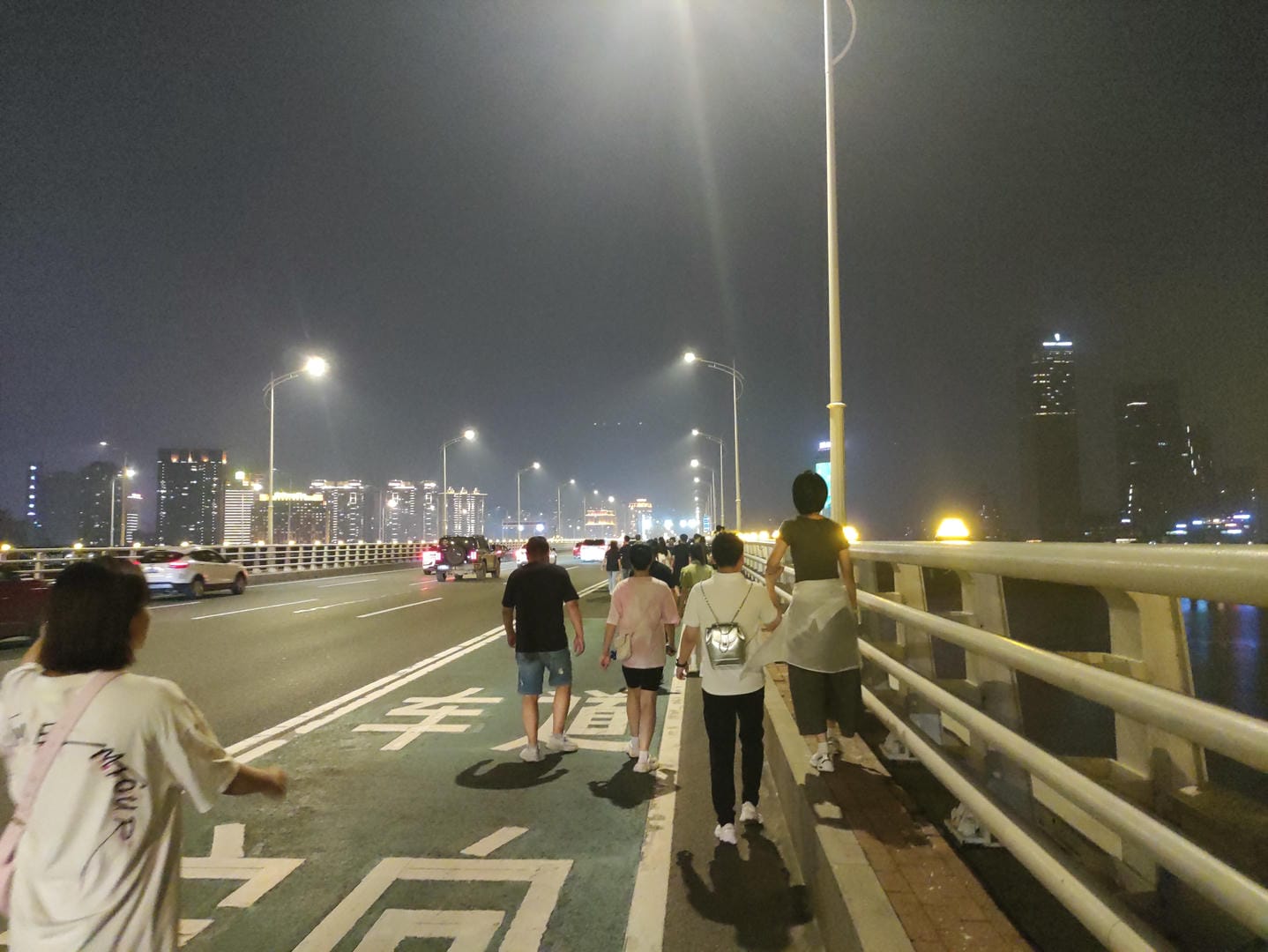 people walking on a bridge at night with a city in the background